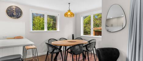 A modern kitchen with a round wooden table, black chairs, a large clock, and a hanging pendant light.