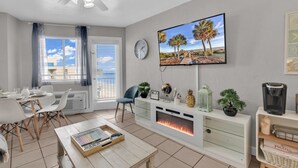 A living room with a fireplace, a TV mounted on the wall, a dining area with a table and chairs, and a window with curtains.