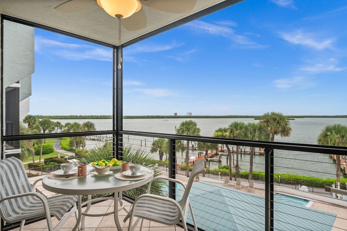 A balcony with a table, chairs, and a view of a body of water.