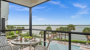 A balcony with a table, chairs, and a view of a body of water.