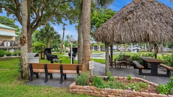 A park area with a thatched-roof pavilion, picnic tables, and benches.