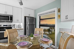Een moderne keuken met witte kastjes, roestvrijstalen apparatuur en een eethoek met een glazen tafel en stoelen.