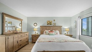Une chambre à coucher avec un lit en bois, une commode, deux tables de chevet avec des lampes et un grand miroir.