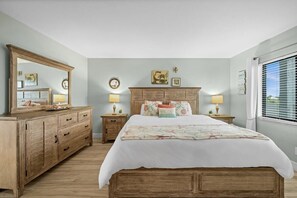 Ein Schlafzimmer mit einem hölzernen Bett, einem Schminktisch, zwei Nachttischen mit Lampen und einem großen Spiegel.