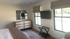 Une chambre à coucher avec un lit, une commode, un miroir, une télévision et des fenêtres.