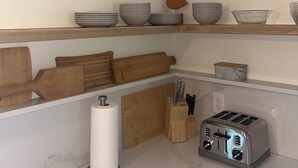 Une cuisine aux murs blancs, dotée d’un plan de travail en marbre, d’une planche à découper en bois, d’un grille-pain et d’un égouttoir à bols.