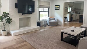 Un salon moderne avec une cheminée, un téléviseur fixé au mur, un pouf rond de couleur grise et une table basse.