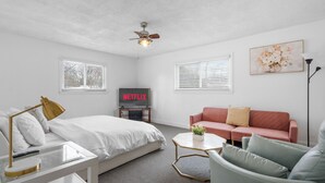 Une chambre d’hôtel moderne équipée d’un lit, d’un canapé, d’une table basse et d’un téléviseur affichant le logo « NETFLIX ».