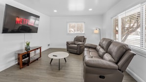 Un salon moderne doté d’un grand téléviseur à écran plat, d’un canapé en cuir, d’un fauteuil inclinable et d’une petite table basse.