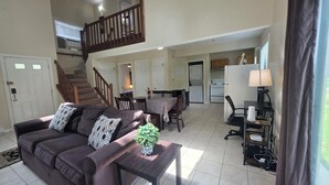 A spacious living area with a sofa, coffee table, and a dining table with chairs. A staircase leads to an upper level. - Family and Workation Retreat (Tobyhanna)