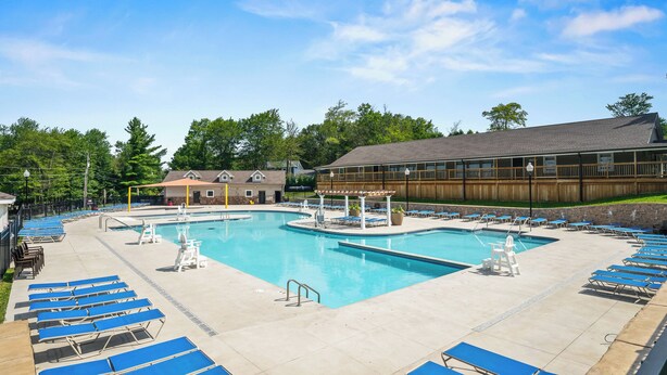 A large outdoor swimming pool with multiple lanes, surrounded by blue lounge chairs and a covered area with a wooden deck. - Family and Workation Retreat (Tobyhanna)