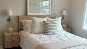 Una camera da letto ordinata con un letto grande, due comodini, un quadro incorniciato sopra il letto e una finestra a destra.