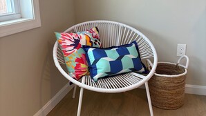 Una sedia in vimini bianco con cuscini colorati, un cesto di vimini e una finestra con vista.
