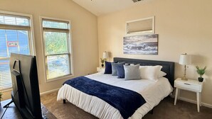 Une chambre à coucher avec un lit, deux tables de chevet avec des lampes, un ventilateur de plafond et un téléviseur posé sur un meuble.