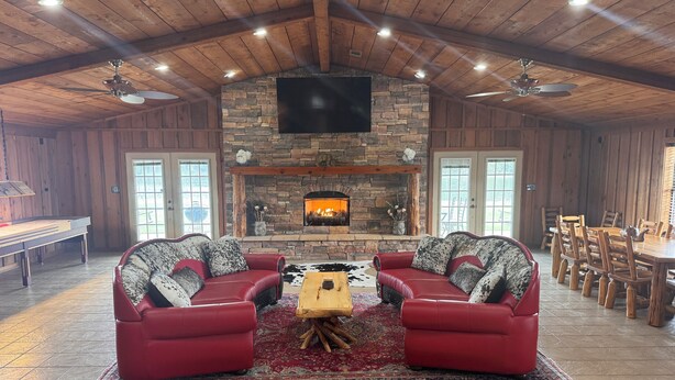 A spacious living room with a stone fireplace, red leather sofas, and a large TV mounted on the wall.