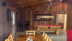A wooden dining area with a pool table and chairs.