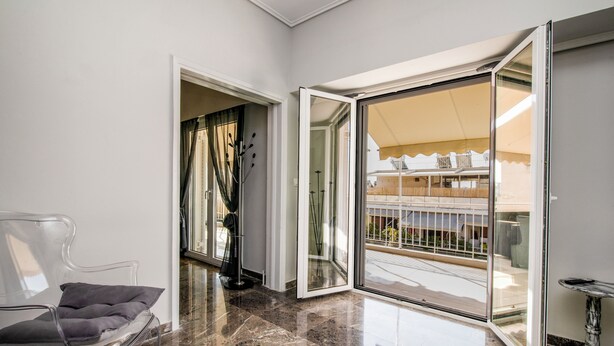Un interior moderno con un vidrio transparente que da a un balcón exterior, una silla transparente y un suelo de mármol.