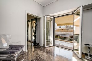 A modern interior with a clear glass door leading to an outdoor balcony, a clear chair, and a marble floor. - Tsil House (Athina)