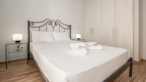 Una cama bien hecha con ropa de cama y toallas blancas, un cabecero de metal y mesitas de noche con lámparas.