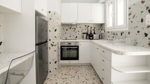 Una cocina moderna con armarios blancos, un refrigerador de acero inoxidable, un horno y una encimera con salpicadero moteado.