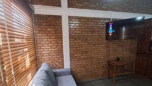 Una stanza con un divano grigio, una parete in mattoni, un tavolo in legno e una TV a muro.