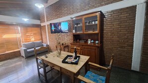 Un accogliente soggiorno con parete in mattoni, un mobile contenitore in legno con ante in vetro, un divano grigio e un tavolo da pranzo in legno con sedie.