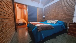 Una stanza con un letto, un comodino, una lampada e un muro in mattoni.