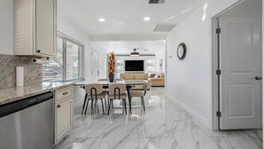 Une cuisine moderne avec des plans de travail en marbre, un coin repas avec une table et des chaises, et un salon avec un canapé et une télévision.