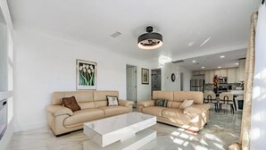 Un salon moderne avec deux canapés beige, une table basse blanche et une cuisine en arrière-plan.