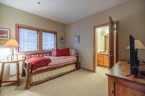 Un dormitorio con una cama de madera, un escritorio, una silla, una lámpara y una puerta que da al baño.