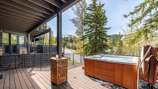 Terraza de madera con jacuzzi y pilar de piedra, con vistas a un área boscosa.