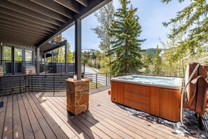 Terraza de madera con jacuzzi y pilar de piedra, con vistas a un área boscosa.
