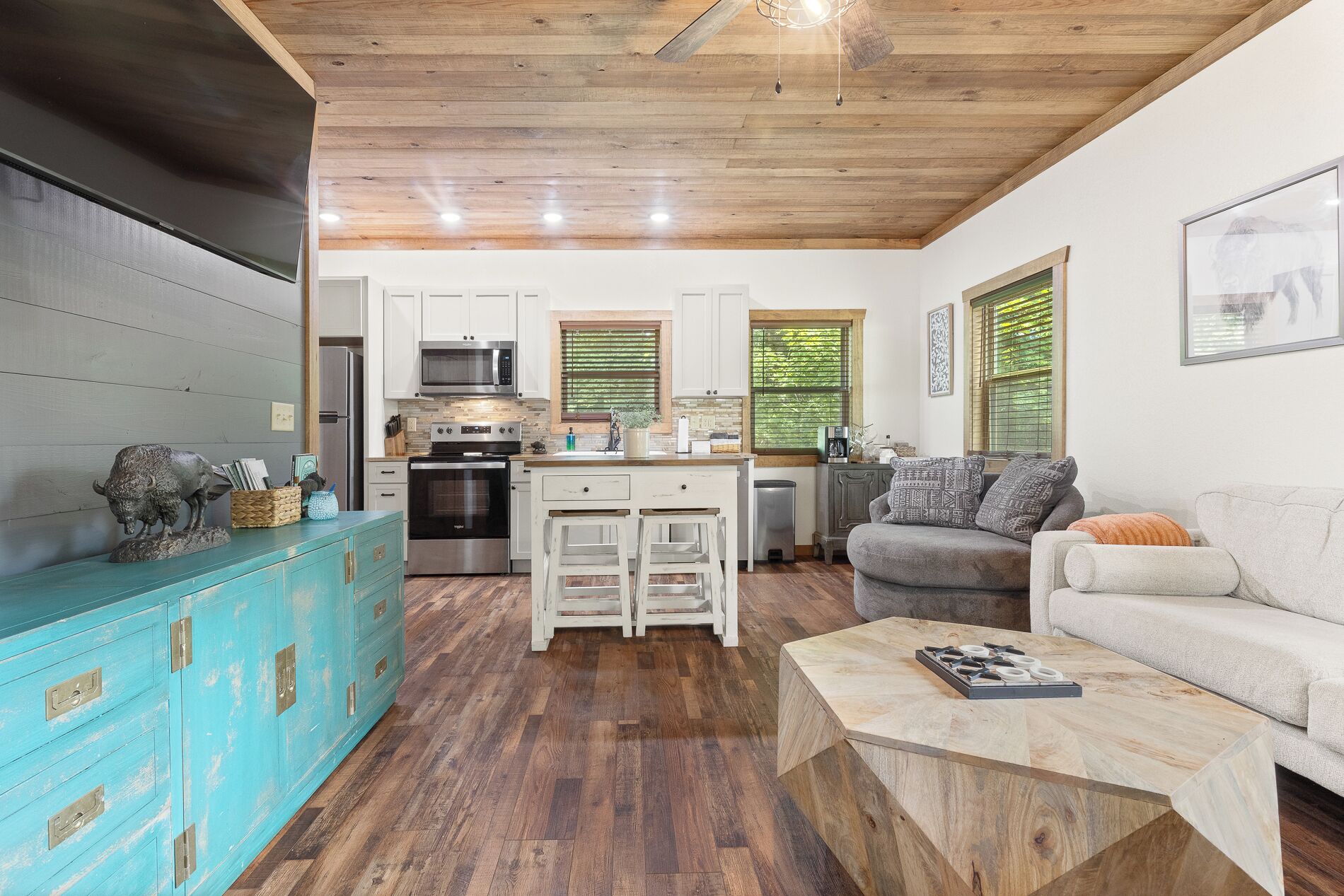 A modern kitchen with white cabinets, stainless steel appliances, and a wooden ceiling.