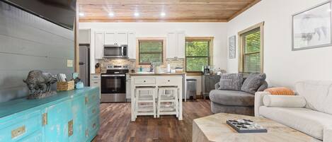 A modern kitchen with white cabinets, stainless steel appliances, and a wooden ceiling.