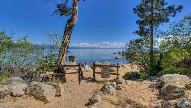 Una playa con un banco de madera, rocas grandes y árboles.