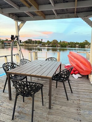 A wooden deck with a table and chairs, a red kayak, and a view of a calm lake with boats and houses in the background. - 1bd/1ba Apartment in St. Petersburg w/PRIVATE DOCK & KAYAKS (St. Petersburg)