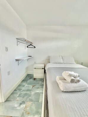 A minimalist bedroom with a bed, a bedside table, a hanging shelf, and a tiled floor. - 1bd/1ba Apartment in St. Petersburg w/PRIVATE DOCK & KAYAKS (St. Petersburg)