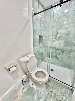 A bathroom with a toilet, a glass shower enclosure, and a marble-tiled wall. - 1bd/1ba Apartment in St. Petersburg w/PRIVATE DOCK & KAYAKS (St. Petersburg)