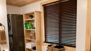 Eine kleine Küche mit Holzausbau, einer integrierten Waschmaschine, einem Holzregal mit Handtüchern und einem Fenster mit Jalousien.