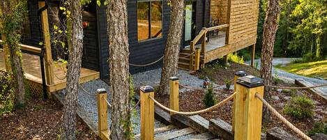 A cabin with a deck, surrounded by trees, and accessible by a wooden staircase.