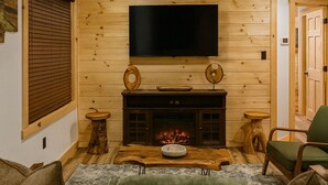 Ein gemütliches Wohnzimmer mit Kamin, Holzwänden, einem Flachbildfernseher und einem grünen Sofa.