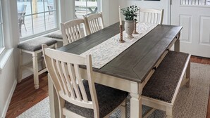 A dining area with a wooden table, white chairs, a chandelier, and large windows overlooking a deck.
