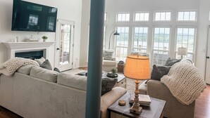 A spacious living room with a fireplace, a large window with a view, and a television mounted on the wall.