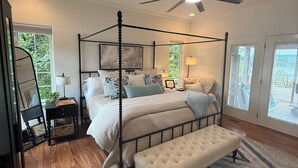 A four-poster bed with a bench, a ceiling fan, and a large window with a view of the outdoors.