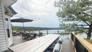 A wooden deck with outdoor furniture, including a table and chairs, overlooking a body of water with trees in the background.