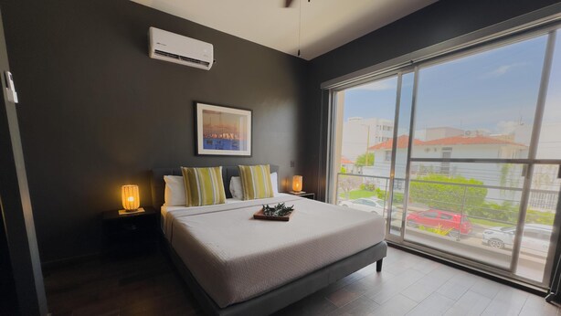 A modern hotel room with a large bed, a city view, and an air conditioning unit. - Modern 2‑Bed Condo in Golden Zone: Walk Everywhere! (Mazatlan)