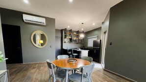 A modern kitchen with a central island, a dining area with a wooden table and chairs, and a large mirror on the wall. - Modern 2‑Bed Condo in Golden Zone: Walk Everywhere! (Mazatlan)