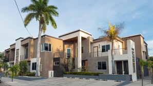 A modern multi-story residential building with balconies, a parking area, and palm trees. - Modern 2‑Bed Condo in Golden Zone: Walk Everywhere! (Mazatlan)