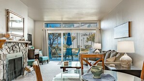 Un salon avec une cheminée, une table basse en verre, un canapé et une vue sur l’extérieur.
