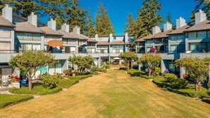 Une rangée d’immeubles modernes à plusieurs étages, avec un chemin central, entourée de pelouses et d’arbres bien entretenus.